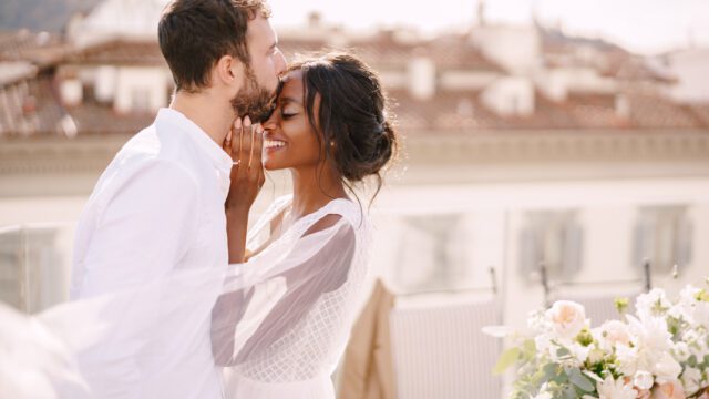 Destination fine-art wedding in Florence, Italy. Caucasian groom and African-American bride cuddling on a rooftop in sunset sunlight. Multiracial wedding couple